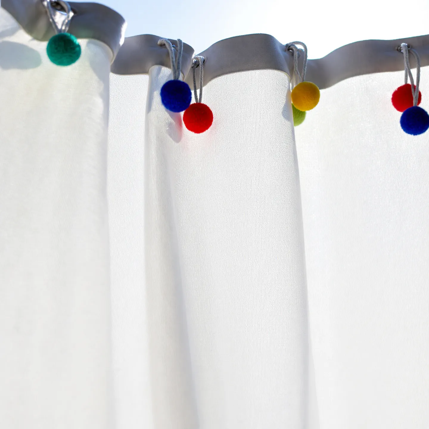 close-up of white curtains with colorful pom-poms attached, glowing in natural light