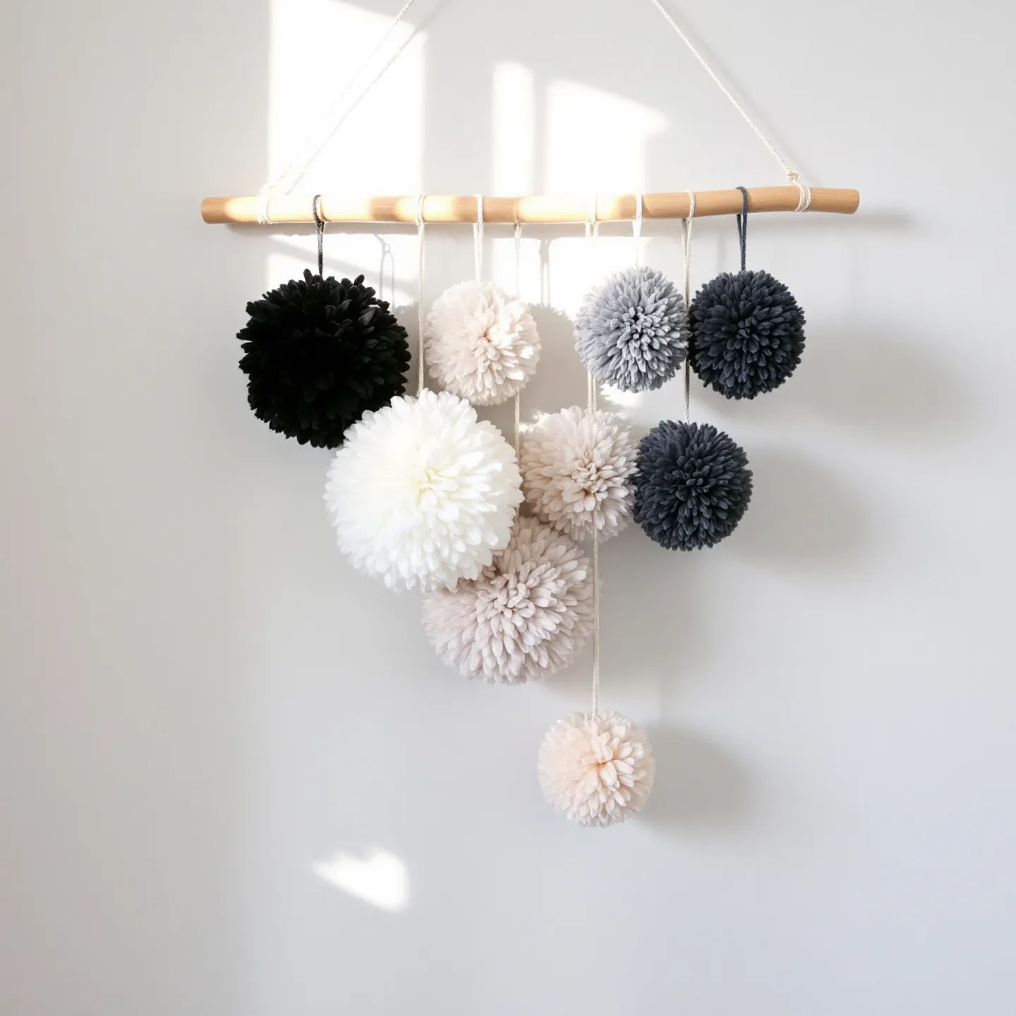 photo of a chic wall hanging made from neutral pom-poms, with an elegant wooden dowel on a light-colored wall