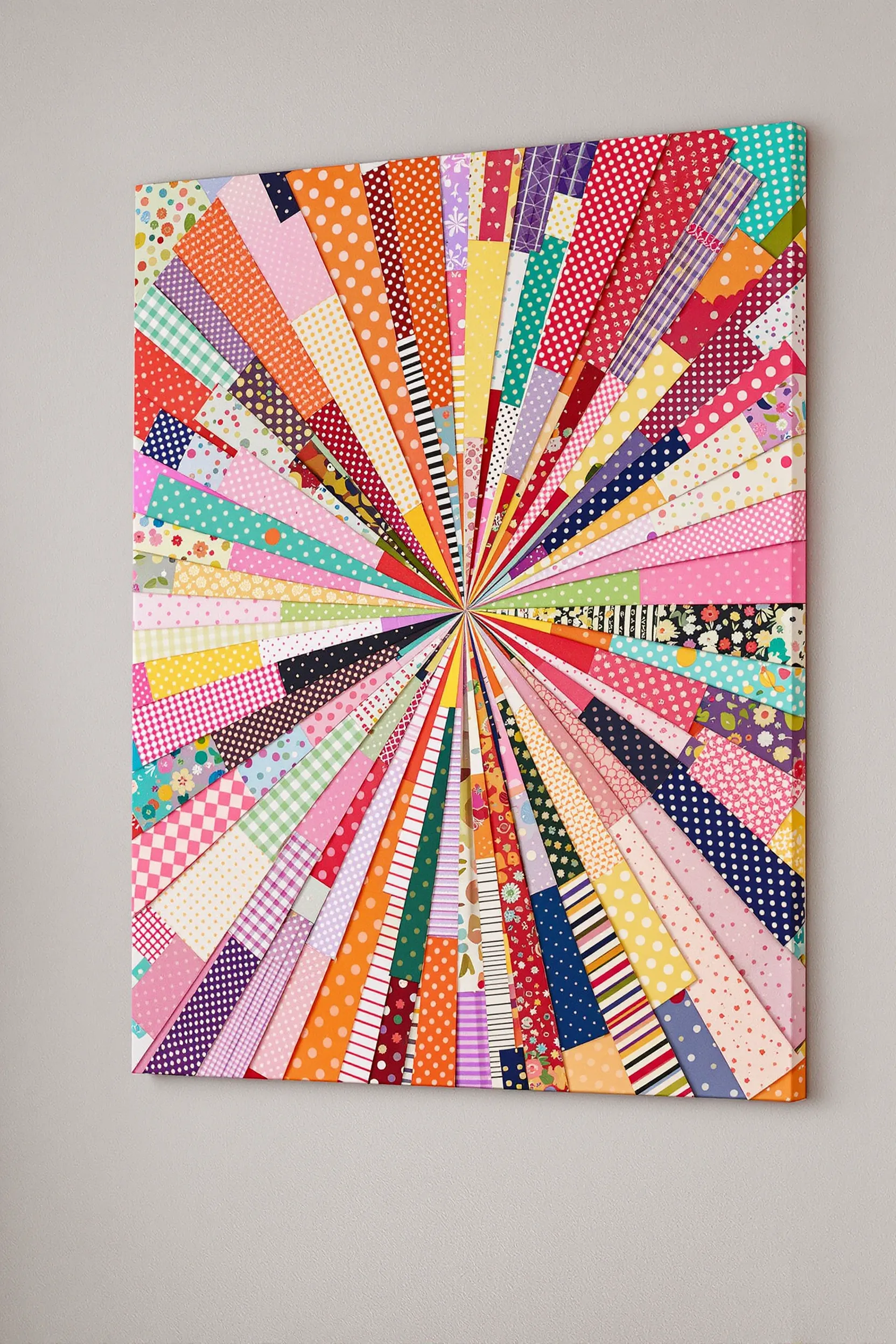 A canvas covered with a colorful fabric scrap collage against a wall